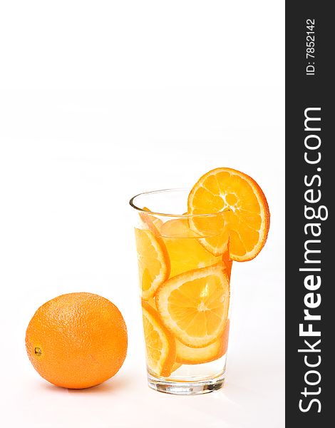 A drinking glass of orange slices and whole orange on white.