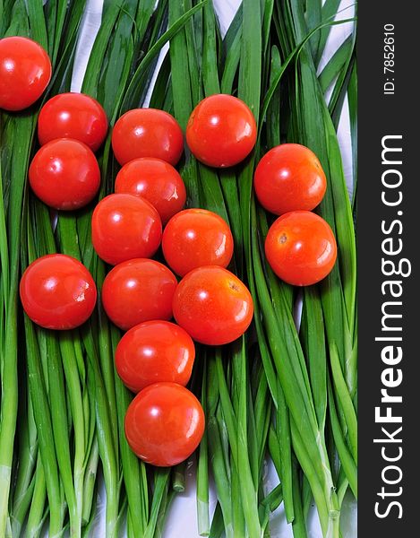 Red cherry tomatoes laying out on baby green onions.