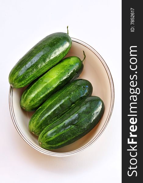 Four fresh green cucumbers in a white dish.