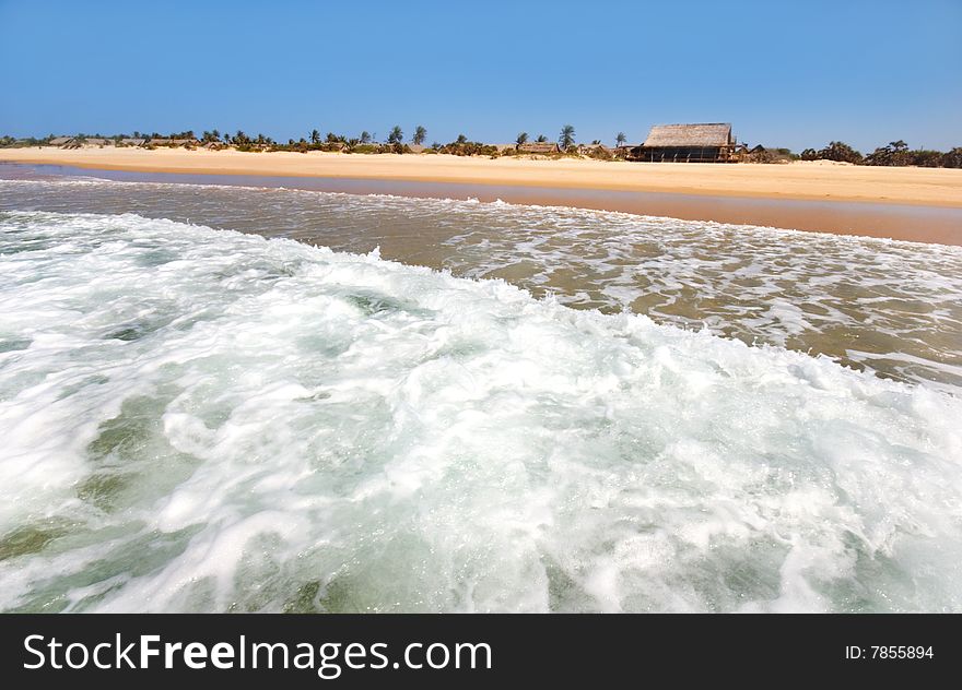 Beach cottage on the sand at surf edge,foamy waves blue sky