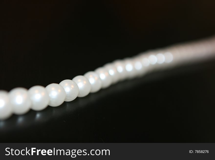 Pearl necklace lying on black table with reflection