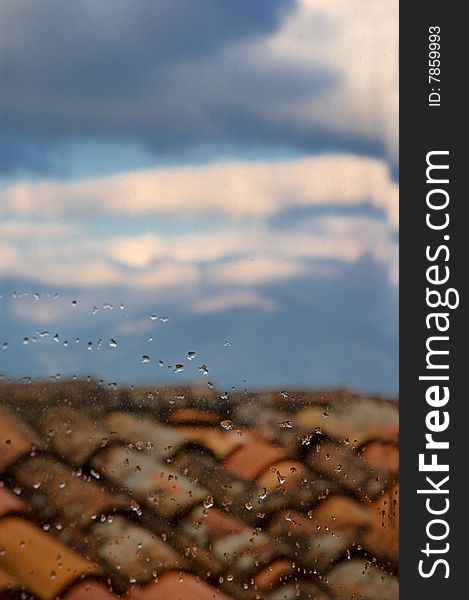 Water drops on window pane with roof and clouds in the distance. Shallow depth of field and copy space. Water drops on window pane with roof and clouds in the distance. Shallow depth of field and copy space.