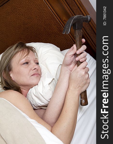 A tired woman in bed holding a hammer ready to strike. A tired woman in bed holding a hammer ready to strike