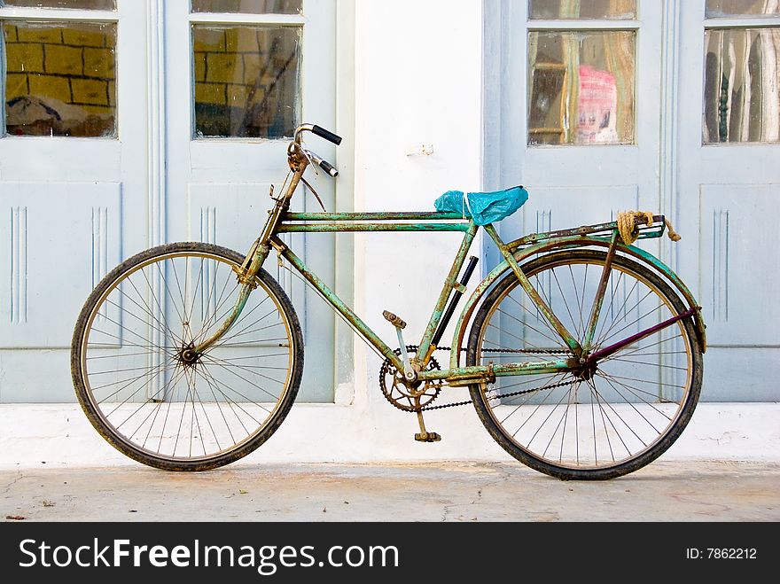 Old rusty green bike standing in front of a white wall with two blue doors. Old rusty green bike standing in front of a white wall with two blue doors
