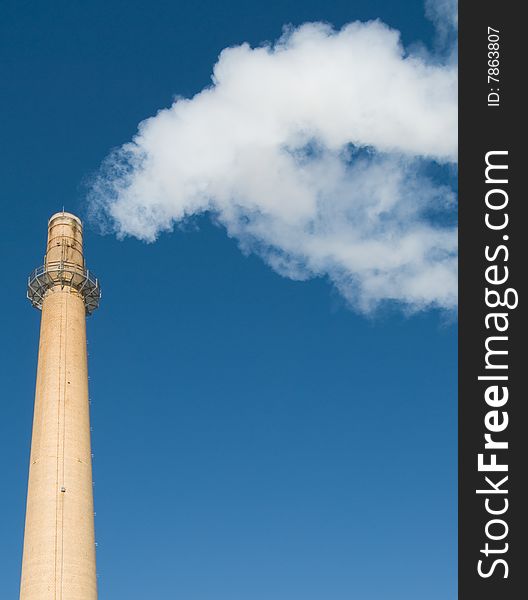 Tall smokestack emitting smoke against a dark blue sky. Tall smokestack emitting smoke against a dark blue sky