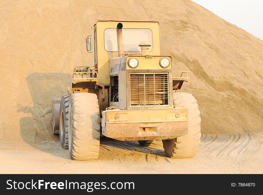 The bulldozer stopped before a sand heap in a construction site. The bulldozer stopped before a sand heap in a construction site.