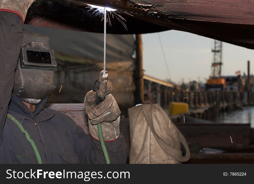 A welder working at shipyard under vessel. A welder working at shipyard under vessel