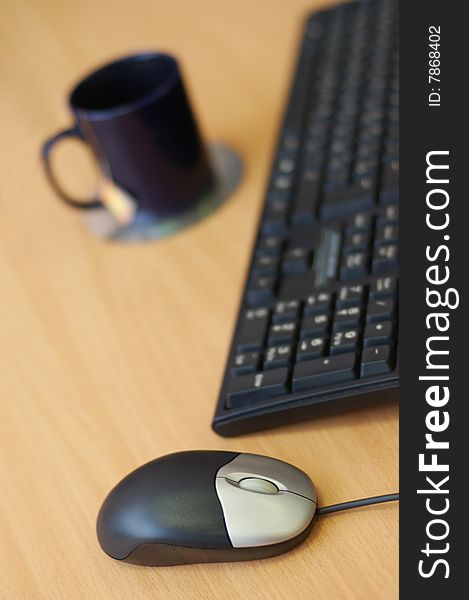 Computer mouse, keyboard and cup on the wooden table. Break for tea