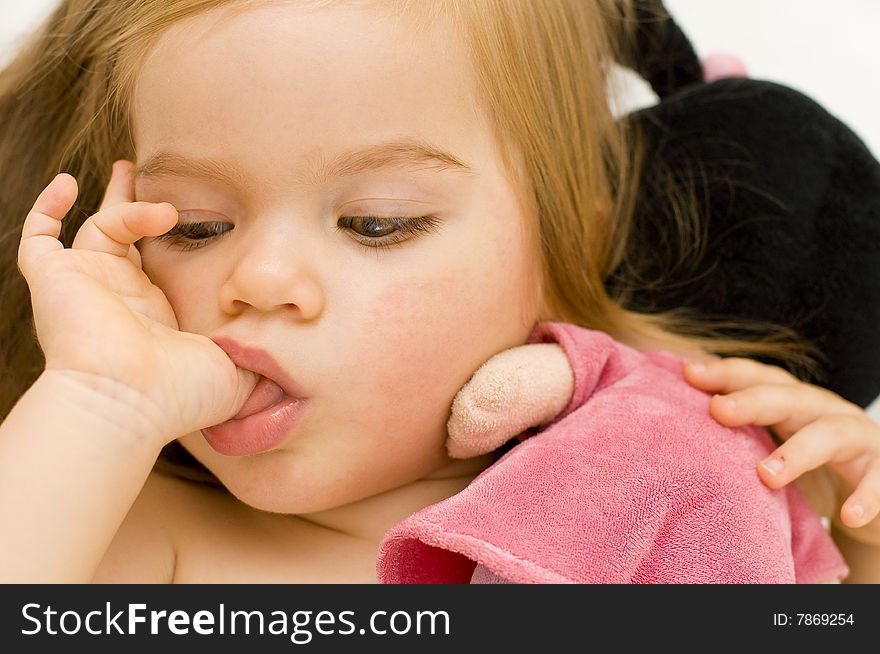 Beautiful baby girl sucking on her thumb and hugging her doll in cot just before bedtime