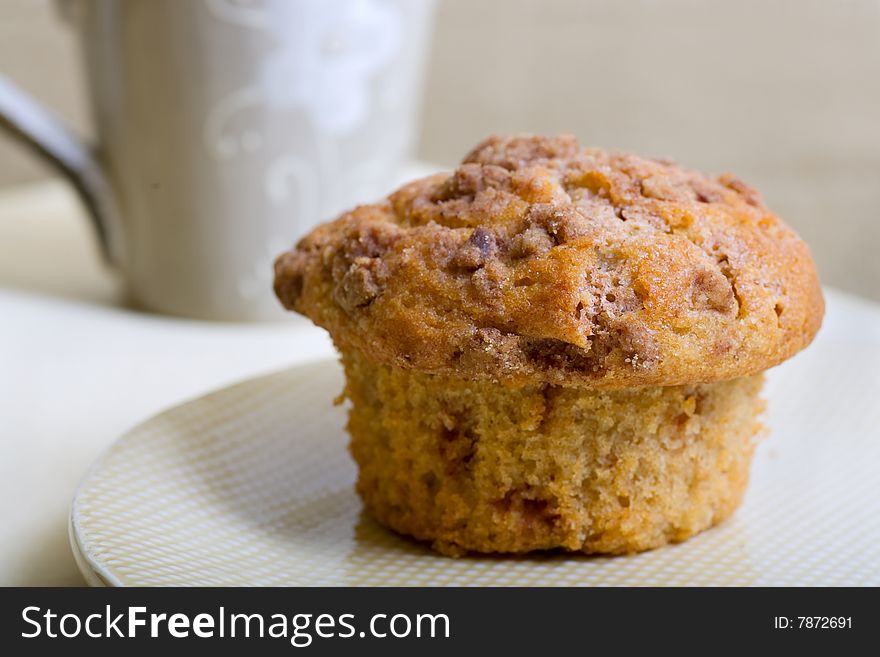 A single cinnamon muffin with a coffee mug in the background