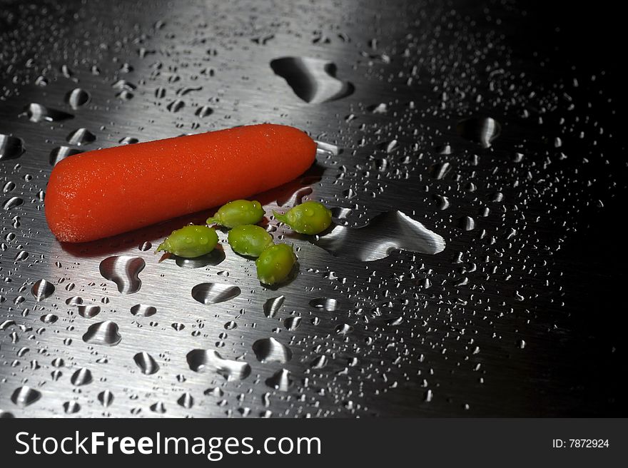 Single baby carrot and a few peas on a silver sheet with water drops. Single baby carrot and a few peas on a silver sheet with water drops