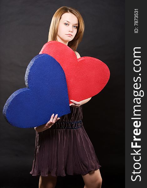 Pretty girl in dress holding two hearts over black background