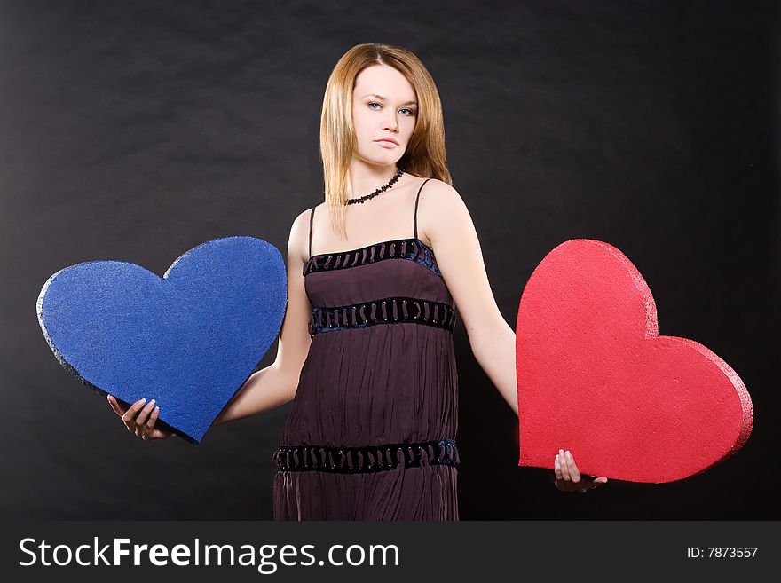 Pretty girl in dress dancing with two hearts  over black background