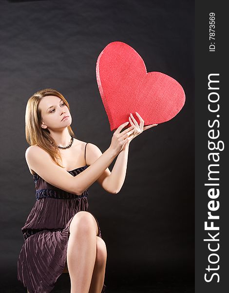 Girl in dress sitting with red heart  over black background