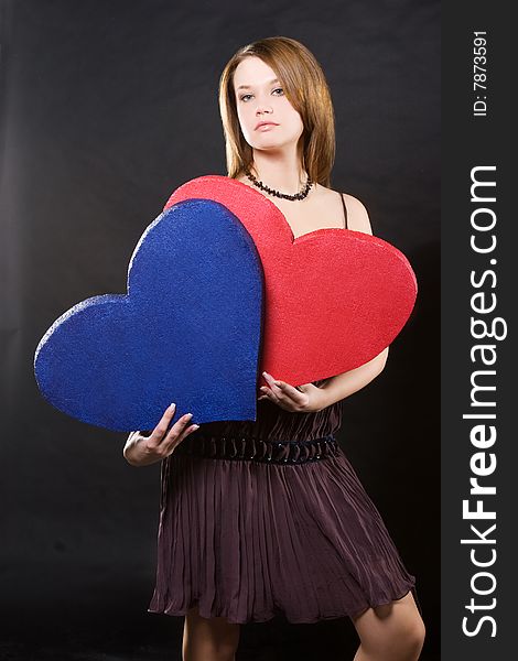 Girl in dress holding two hearts  over black background