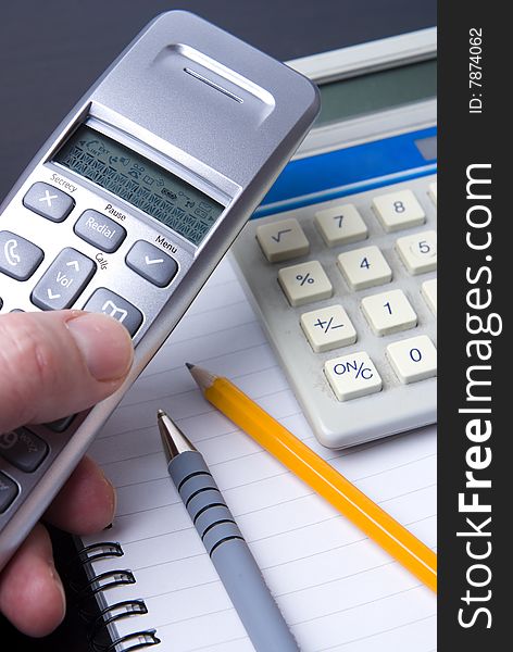 Phone and calculator on a spiral notebook with pen and pencil. Differential focus.