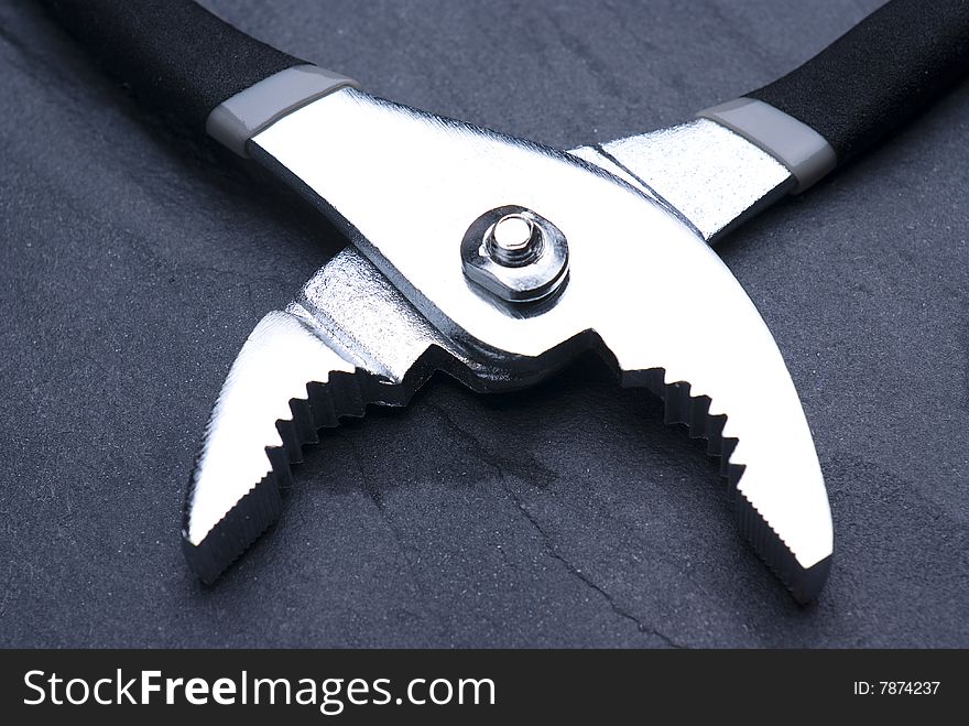 Pair of pliers shot to contrast chrome gleam against slate background. Pair of pliers shot to contrast chrome gleam against slate background