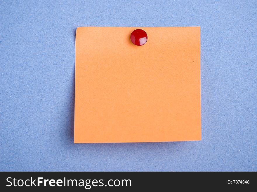 Post it note. Orange with red drawing pin. Isolated on blue background. Post it note. Orange with red drawing pin. Isolated on blue background.