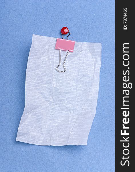 Blank notepaper on blue background crushed and hung from clip held by red drawing pin.