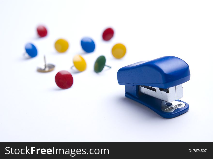 Blue stapler on white background with colorful thumb tacks. Differential focus. Blue stapler on white background with colorful thumb tacks. Differential focus.