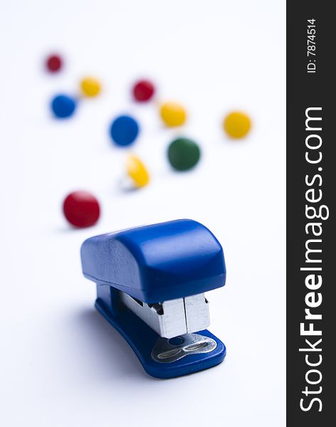 Blue stapler on white background with colorful thumb tacks. Differential focus. Blue stapler on white background with colorful thumb tacks. Differential focus.