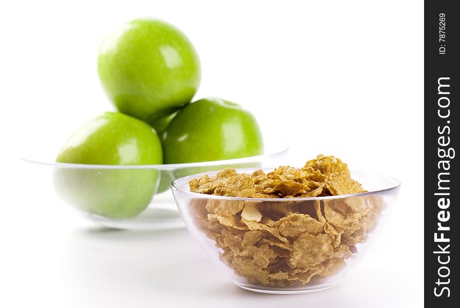 Cornflakes and green apples in glass bowls on white background