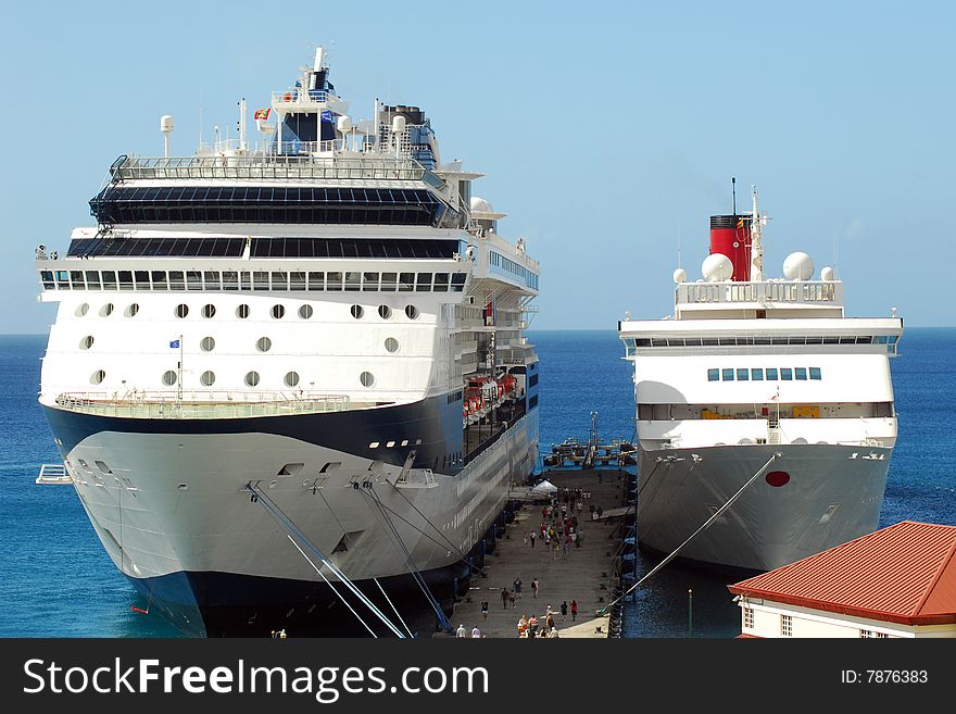 Two cruise ships at dock in Caribbean with passengers walking on dock. Two cruise ships at dock in Caribbean with passengers walking on dock.