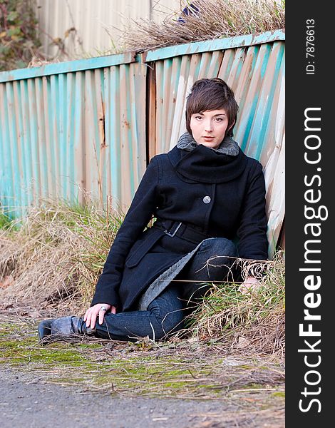A fashion model sits in some grass next to an old rusty wall. A fashion model sits in some grass next to an old rusty wall.