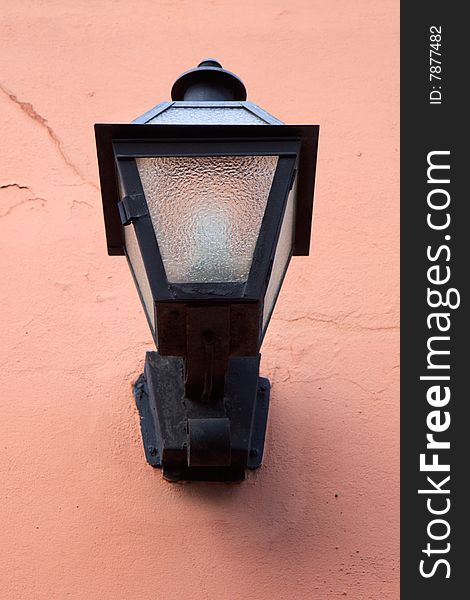 Antique gas lamp against a peach colored wall; in vertical orientation