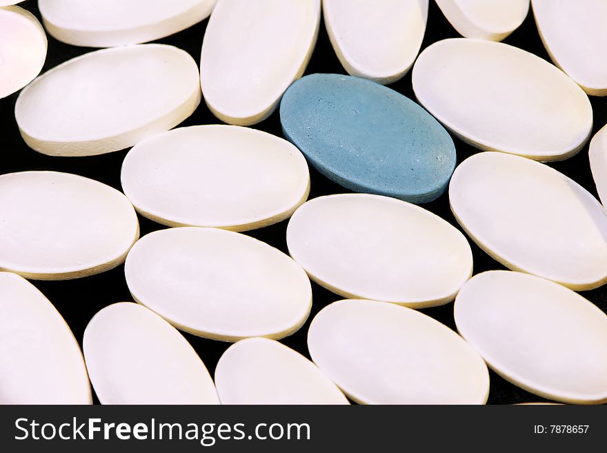 Macro shot of white pills with one blue pill.