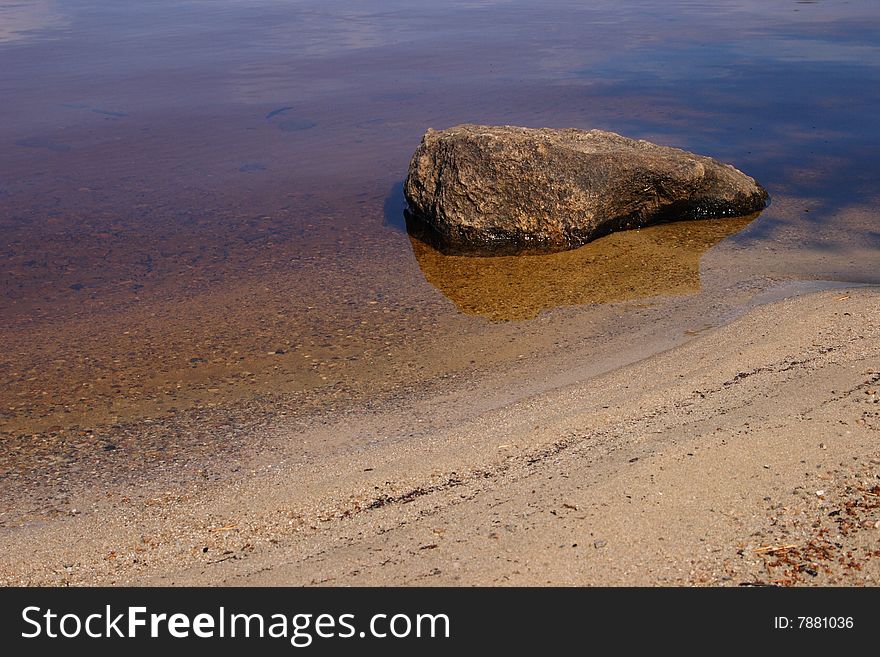 The big stone lies in water on the bank of lake.