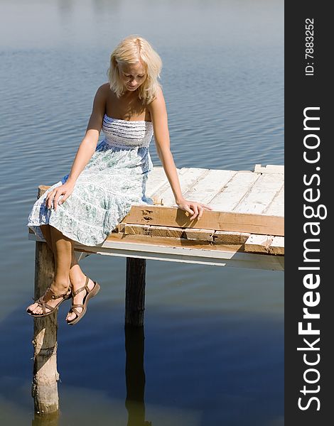 Girl sitting on a pier, looking into the water