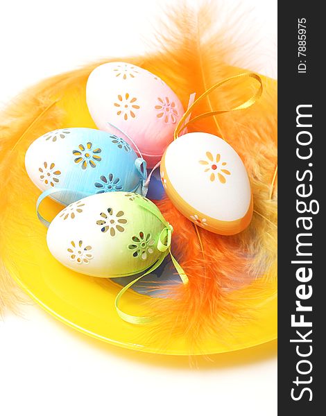 Easter eggs on yellow plate with yellow and orange feathers.