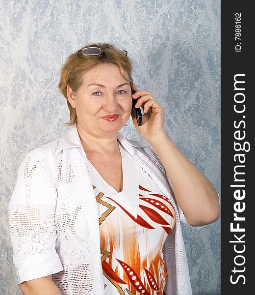 The mature woman talks by a mobile phone. The mature woman talks by a mobile phone