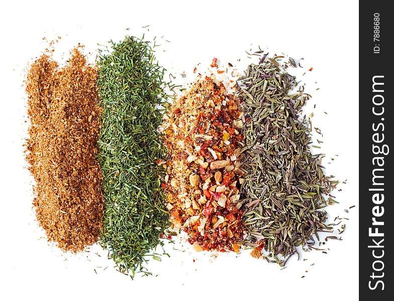 Various spices lying in four heaps on white background