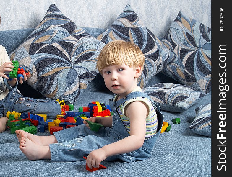 The little boy plays toys sitting on a sofa. The little boy plays toys sitting on a sofa