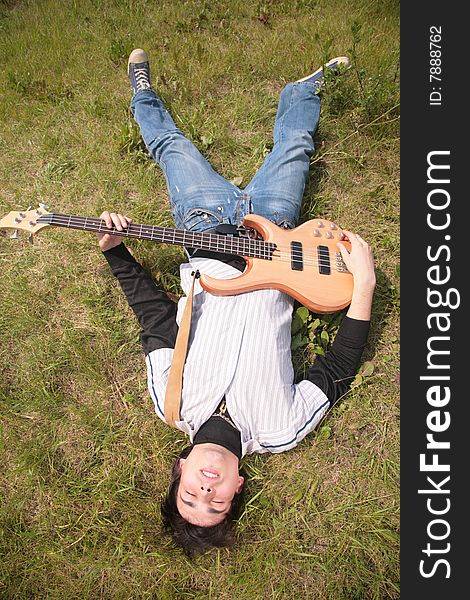 Young man  lies with guitar on grass