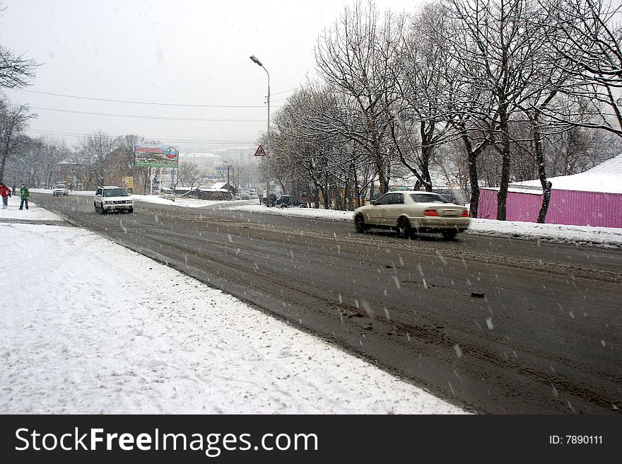Motor vehicles go on slippery dangerous road on background of the snowfall