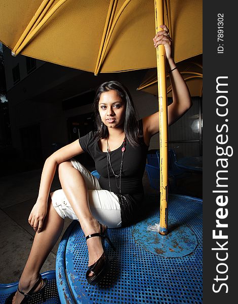 Young woman sitting on a blue table with a yellow metal table umbrella. Young woman sitting on a blue table with a yellow metal table umbrella