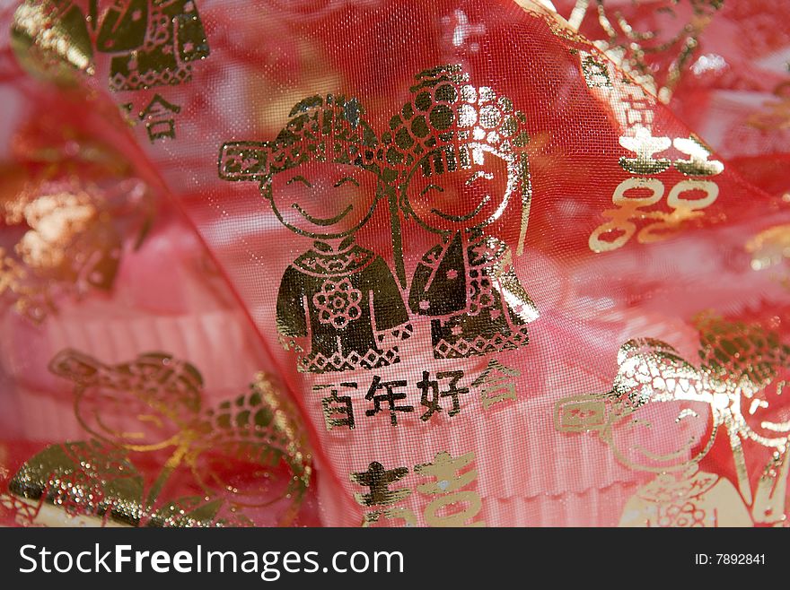 Thin translucent red meshed cloth decorated with gold Chinese characters and figures depicting marriage veiling a pair of heart shaped boxes with ribbons