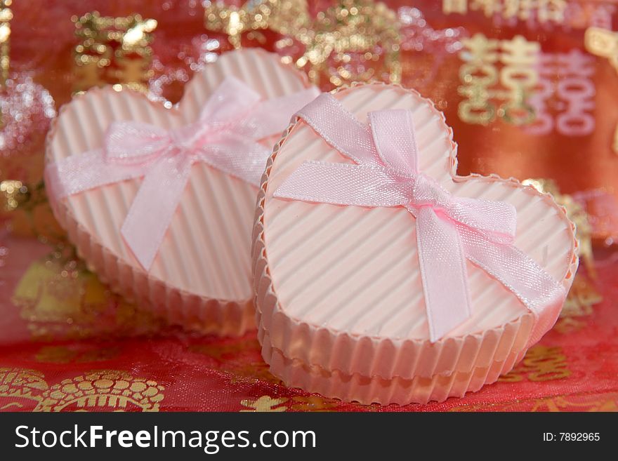 Still life of a pair of heart shaped boxes with ribbons on a red thin cloth decorated with gold Chinese characters and figures depicting marriage. Still life of a pair of heart shaped boxes with ribbons on a red thin cloth decorated with gold Chinese characters and figures depicting marriage