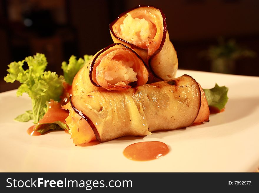 A aubergine roasted and stuffed with rice and trout, accompanies by lettuce and a sauce on a white plate. A aubergine roasted and stuffed with rice and trout, accompanies by lettuce and a sauce on a white plate