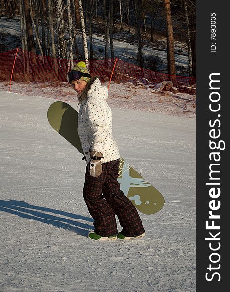 Woman with snowboard walking up snow-covered slope