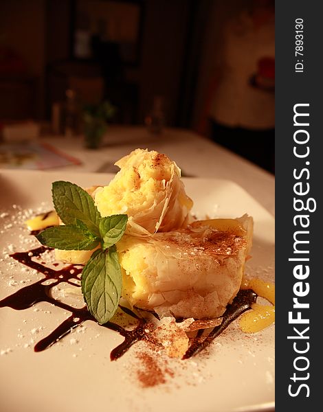 A phyllo custard dessert with chocolate sauce on a white plate accompanied by a peppermint lead and lemon dressing. A phyllo custard dessert with chocolate sauce on a white plate accompanied by a peppermint lead and lemon dressing