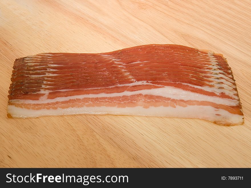 Raw bacon slices on wooden table.