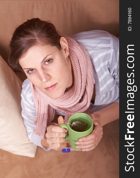 A young woman is sick. She is lying on the couch and is sneezing. She has a tea in her hand. A young woman is sick. She is lying on the couch and is sneezing. She has a tea in her hand.