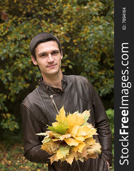 Portrait of a handsome man walking in an autumnal park with a bouquet of mapple leaves. Portrait of a handsome man walking in an autumnal park with a bouquet of mapple leaves