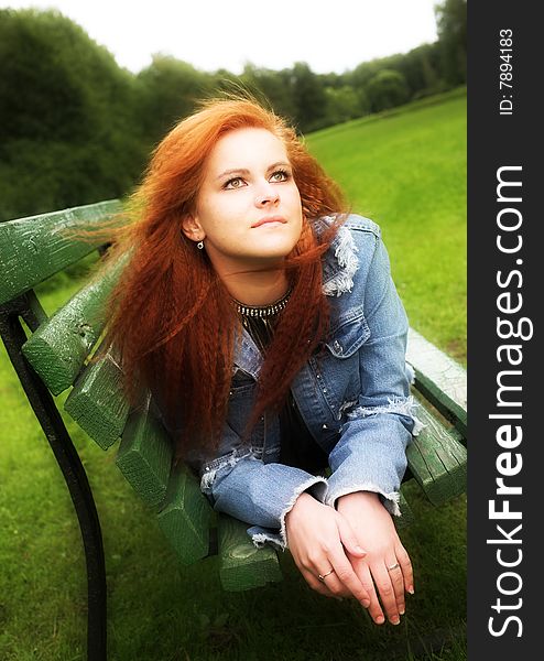 Portrait of a red-haired young woman relaxing on the bench in city-park