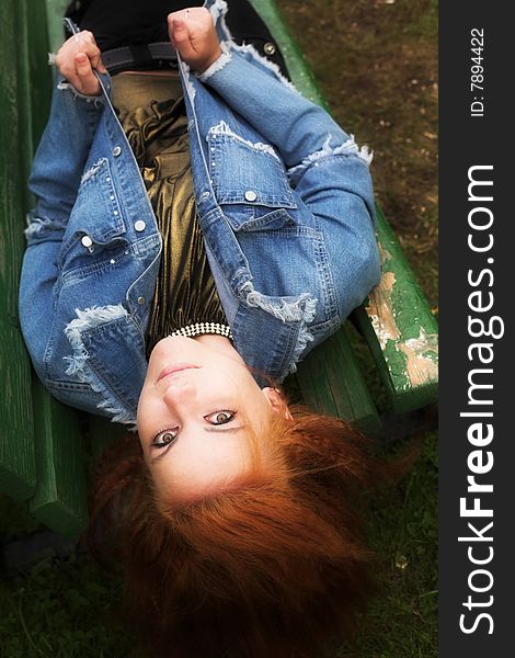 Portrait of a red-haired young woman relaxing on the bench in city-park