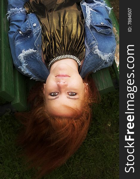 Portrait of a red-haired young woman relaxing on the bench in city-park